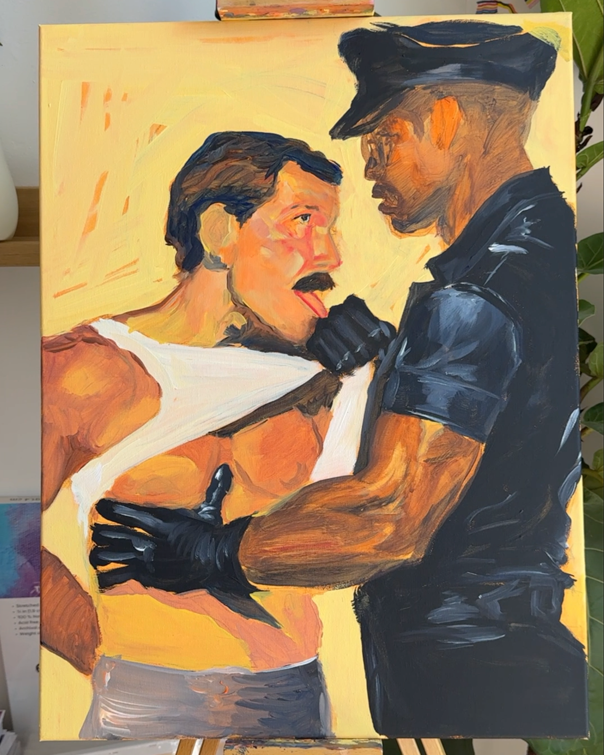 An acrylic painting on canvas depicting a shirtless man with a mustache and a police officer in a black uniform and cap, holding the man's arms. The painting is shown on an easel, with a yellow background and visible brushstrokes throughout.