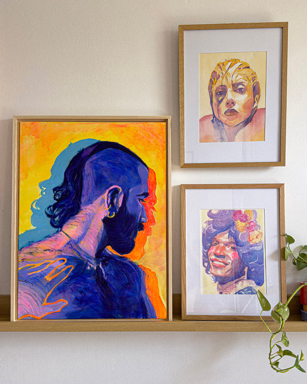 Framed gay and queer art featuring men, with colorful portraits of Marsha P. Johnson and Lady Gaga.